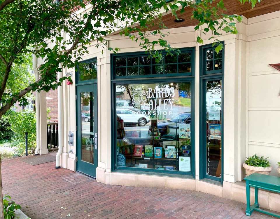 The front of Bards Alley facing Church Street. It shows the front door and large front window, both with a deep green trim. The Bards Alley logo is visible in the window as well as a large shelf of books.