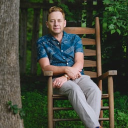a photo of Silas House, a white man with light brown hair, sitting in a rocking chair